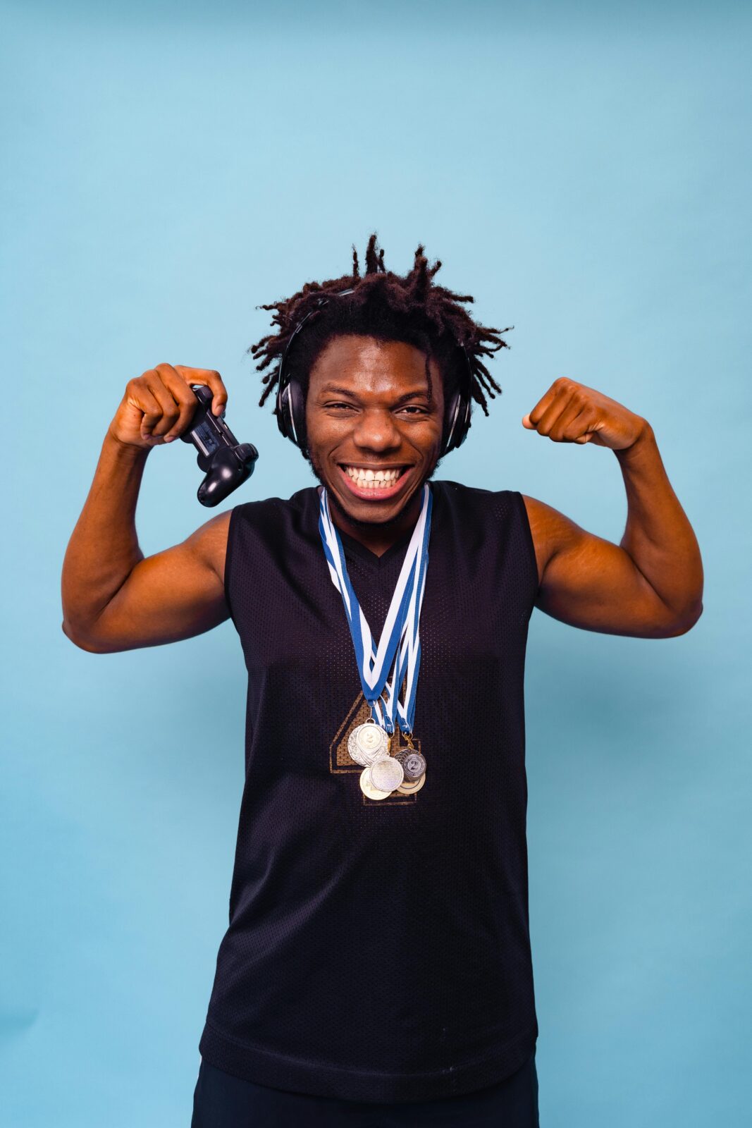 Smiling African American man holding game controller and medals on blue background, celebrating victory.